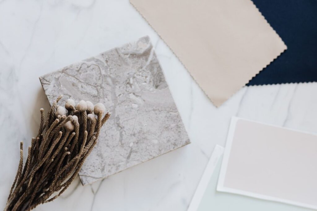 A stylish flat lay of fabric samples, marble slab, and dried florals on a light surface.